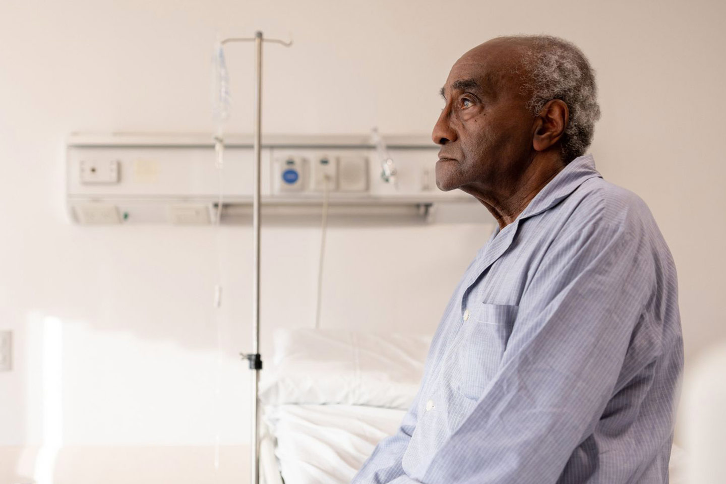 Photo of a man in blue pyjamas sitting on the edge of a hospital bed