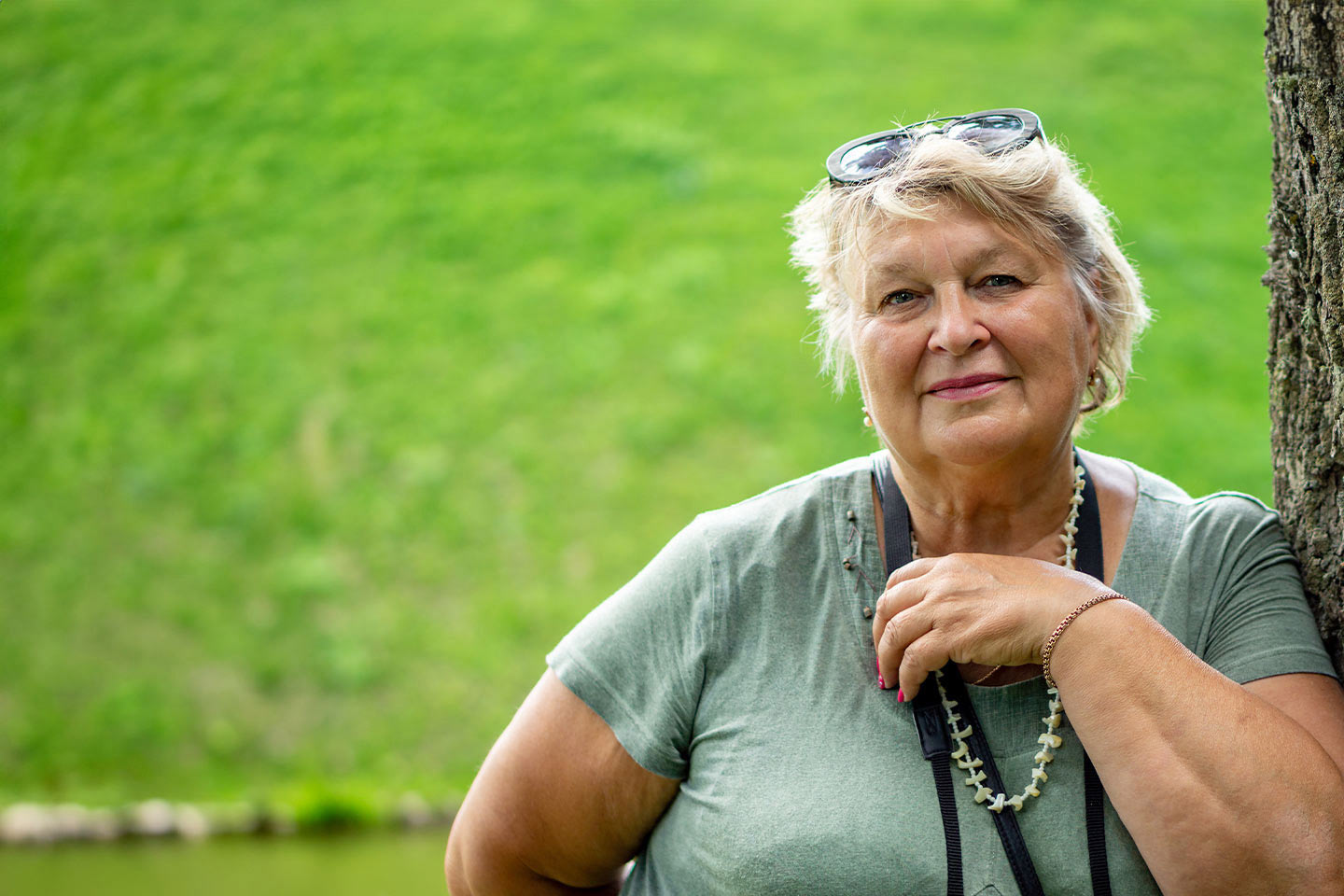 Image of an older Caucasian woman standing outside and leaning against a tree