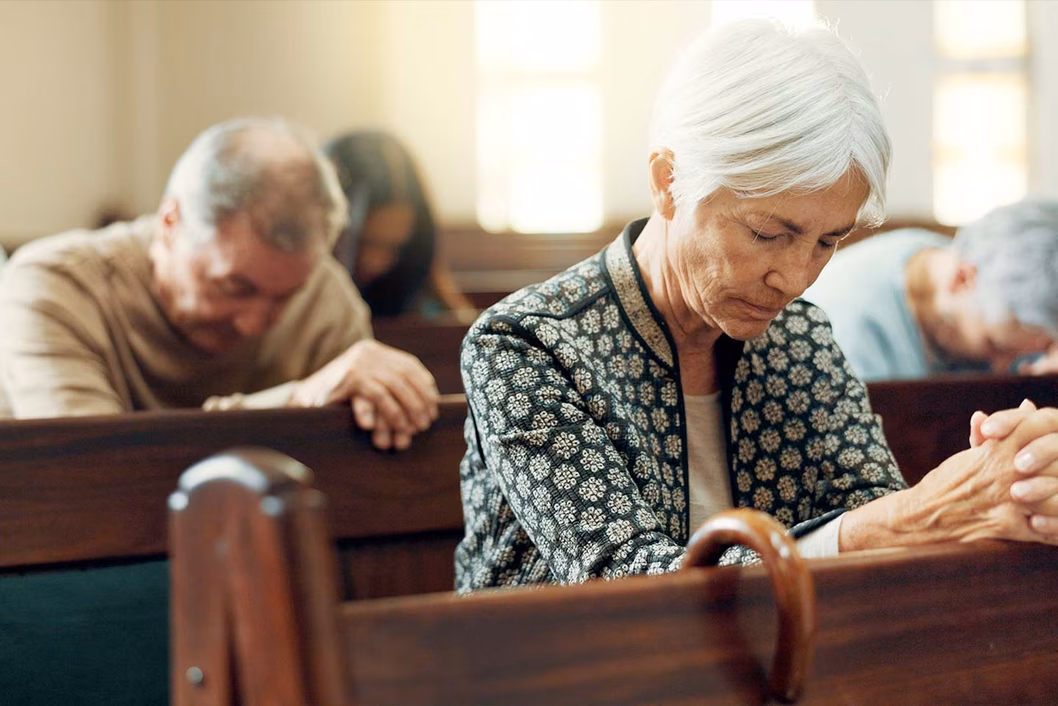 Photo of a woman and three others praying in a church