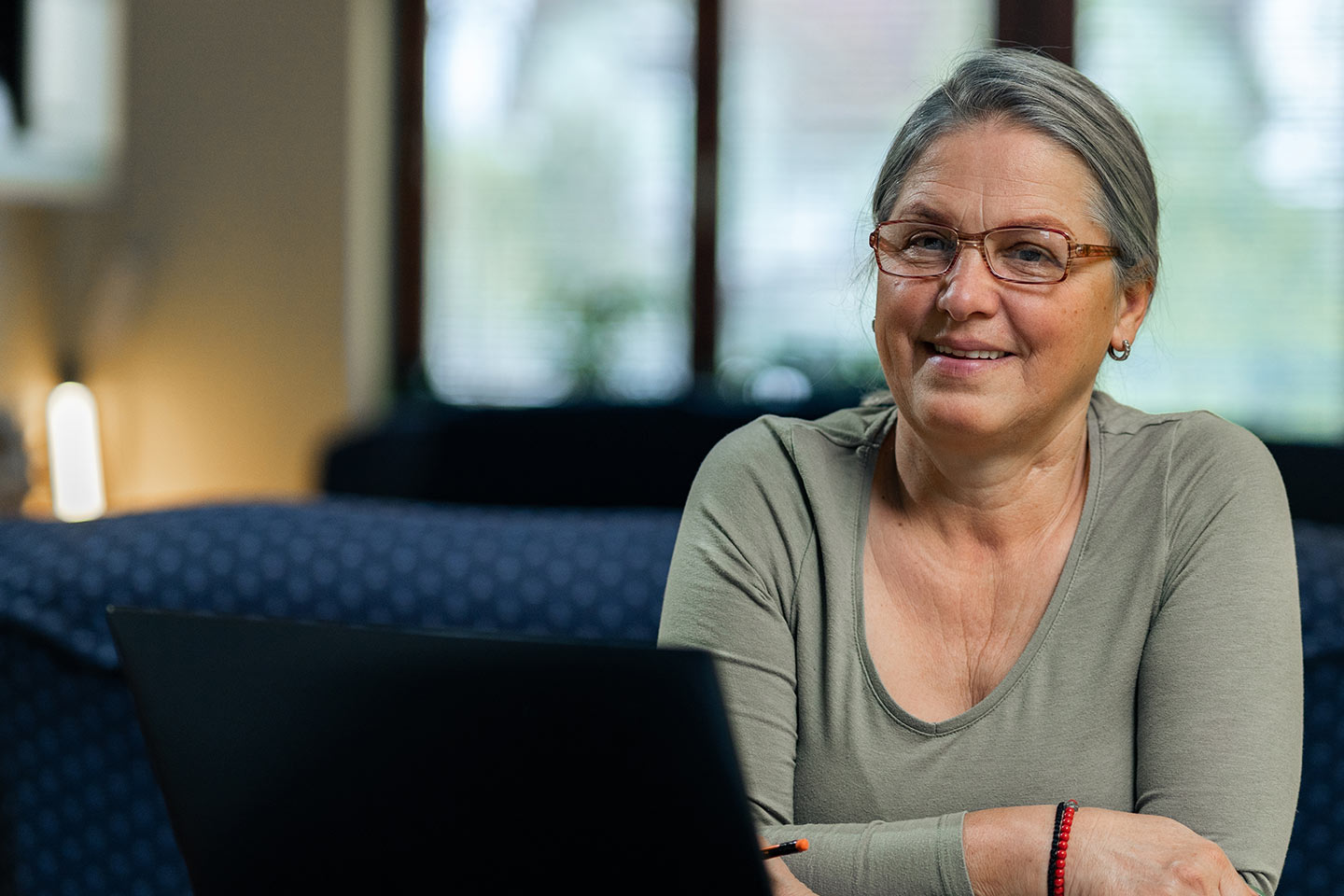 Photo of a woman in a sage green top sitting on a blue couch