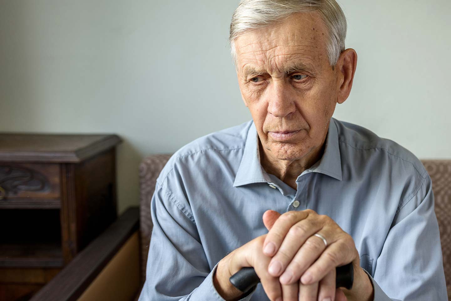 Photo of a seated man resting his hands on a walking stick
