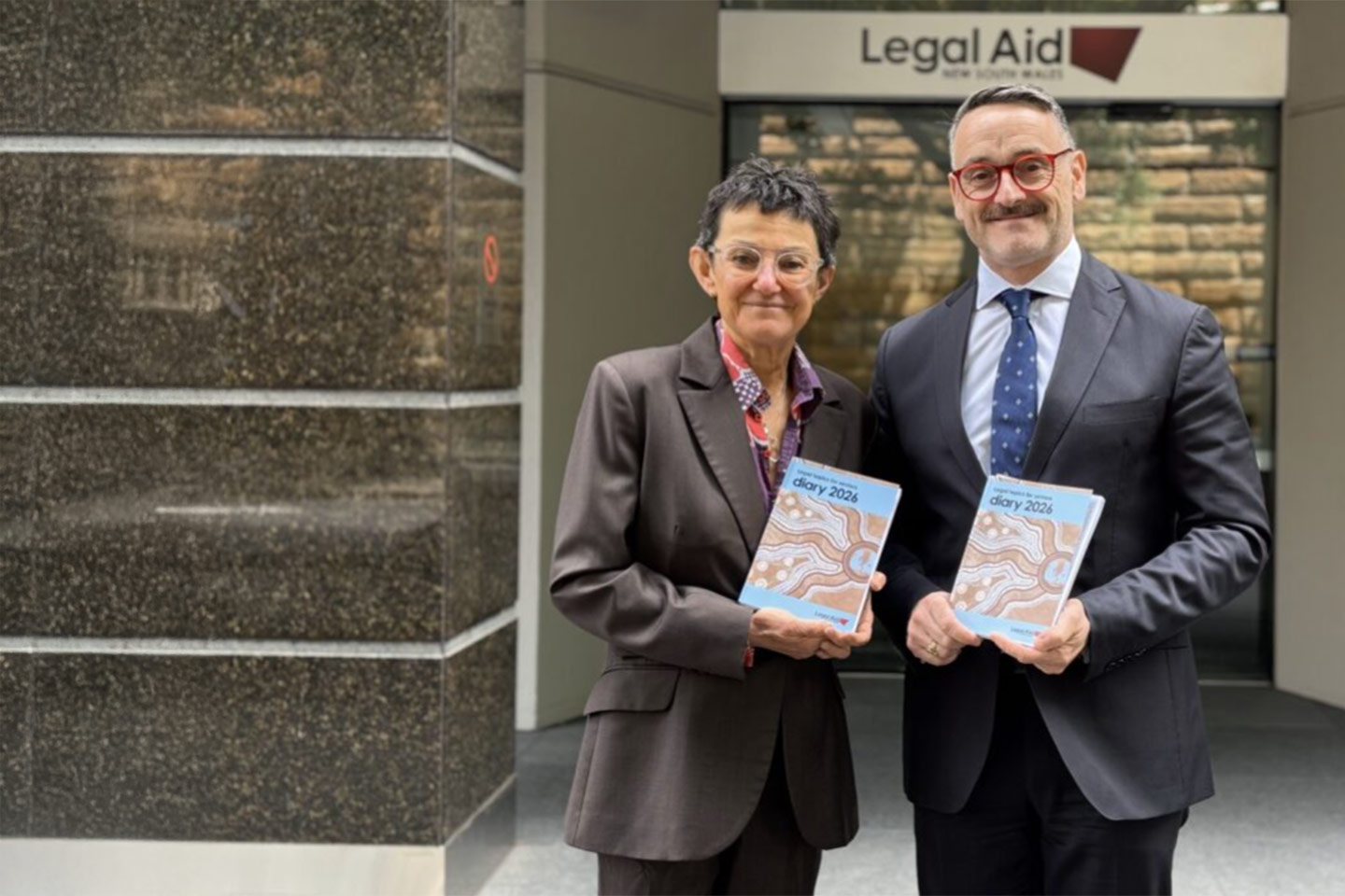 Photo of two people in suits holding books and smiling