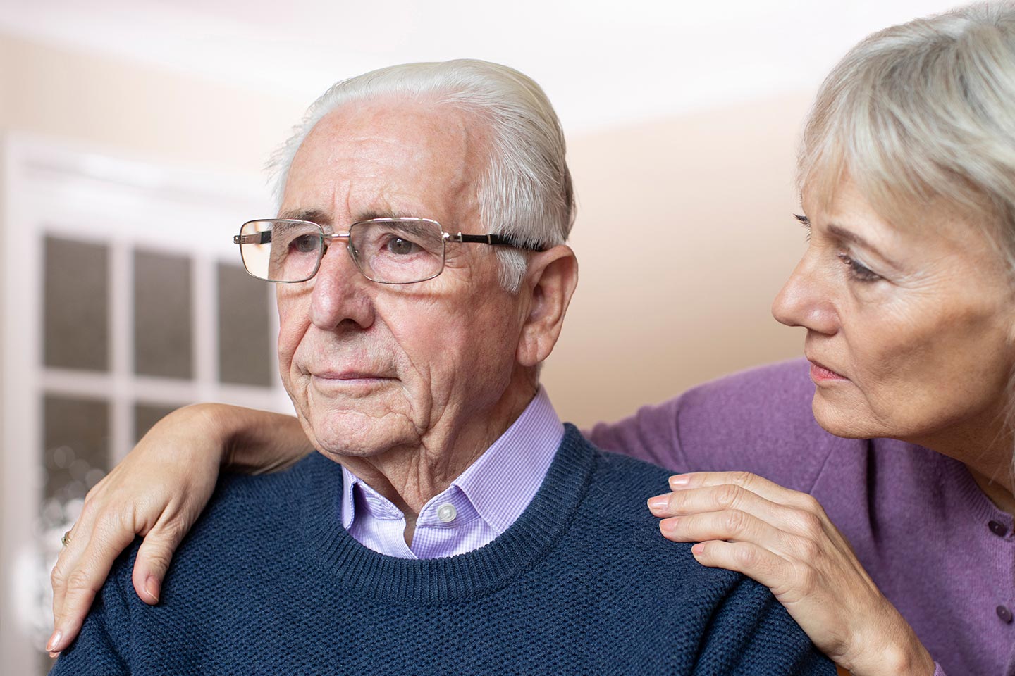 Photo of a woman in a lavender cardigan comforting a man with glasses