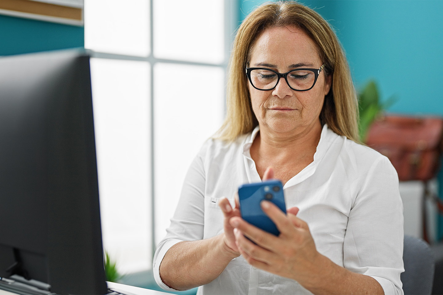 Photo of woman in front of a computer holding a phone