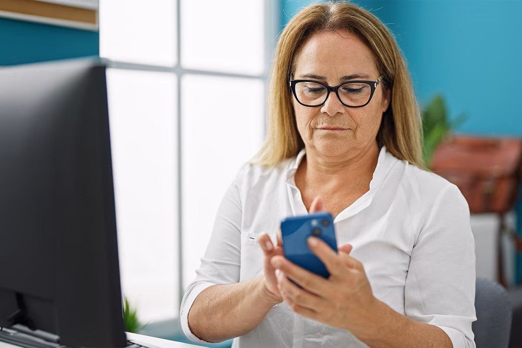 Photo of woman in front of a computer holding a phone