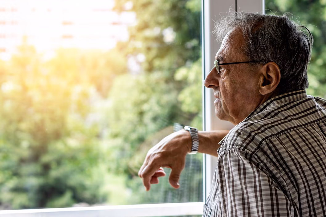 Image of an older Southern European man looking out of a window