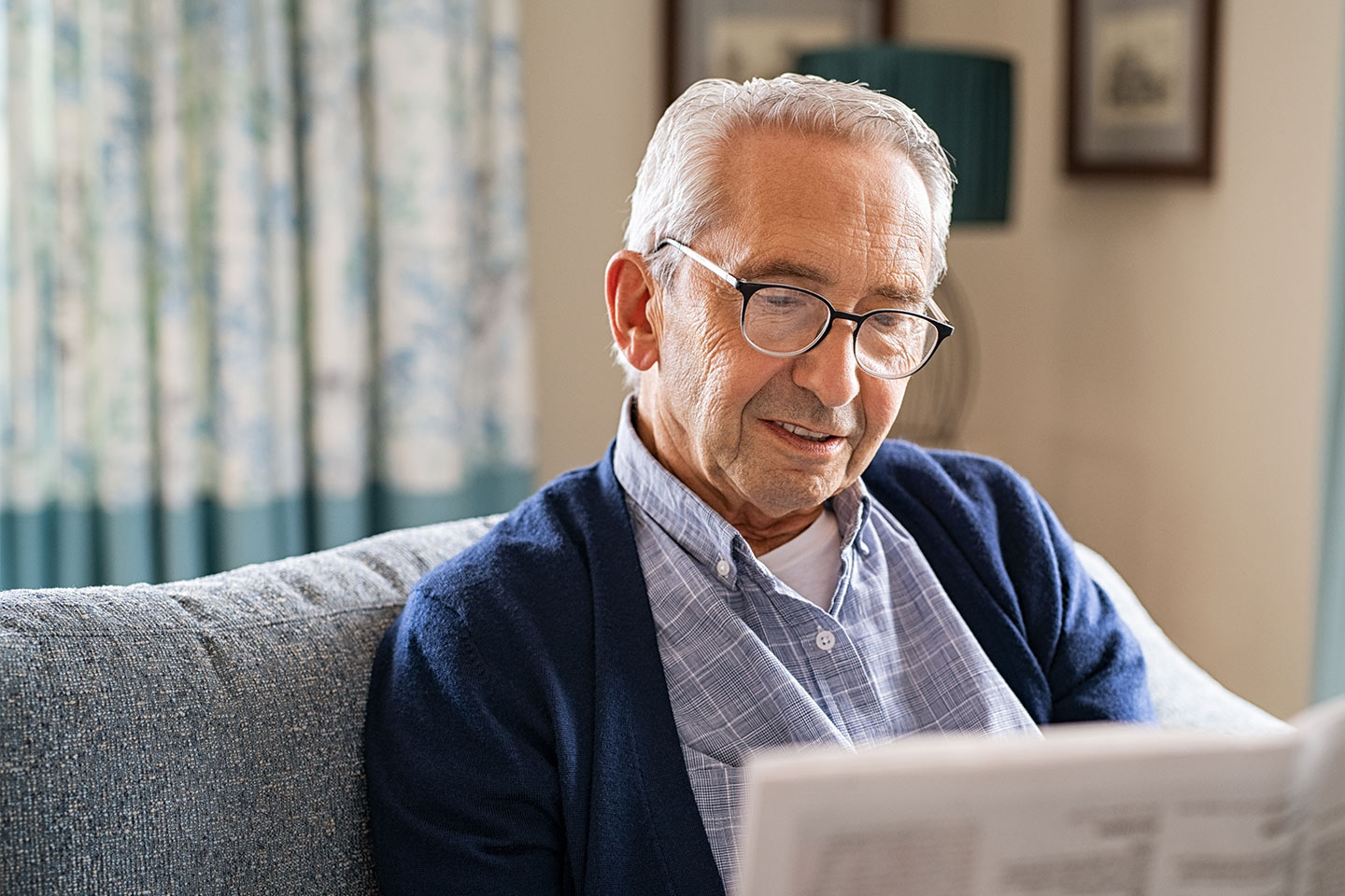 Photo of a man in a blue outfit reading the paper on a couch