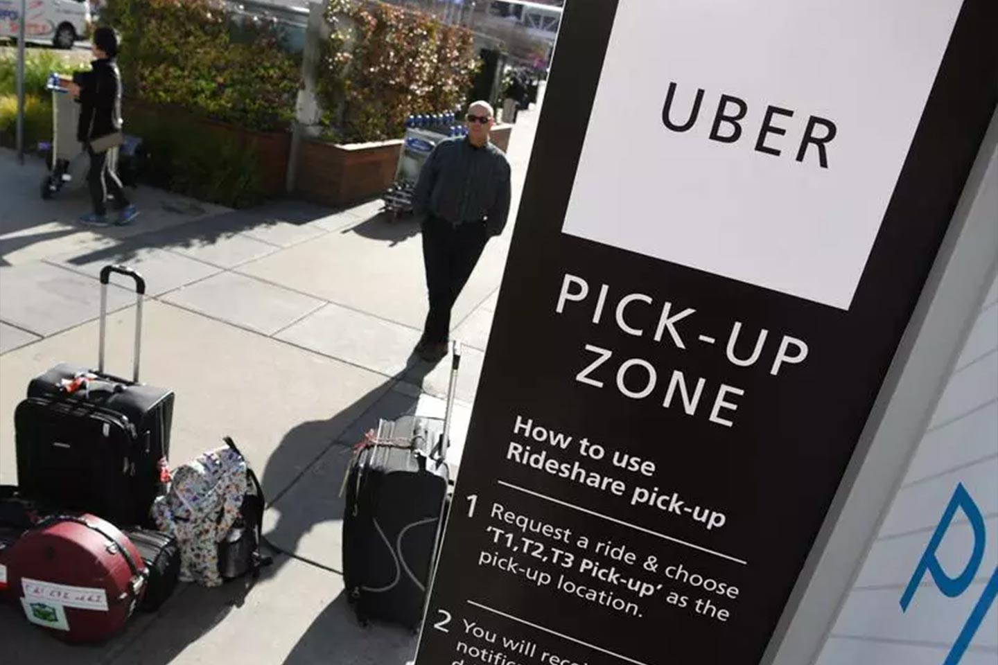 Photo of Uber pickup sign on a street with suitcases and a waiting man