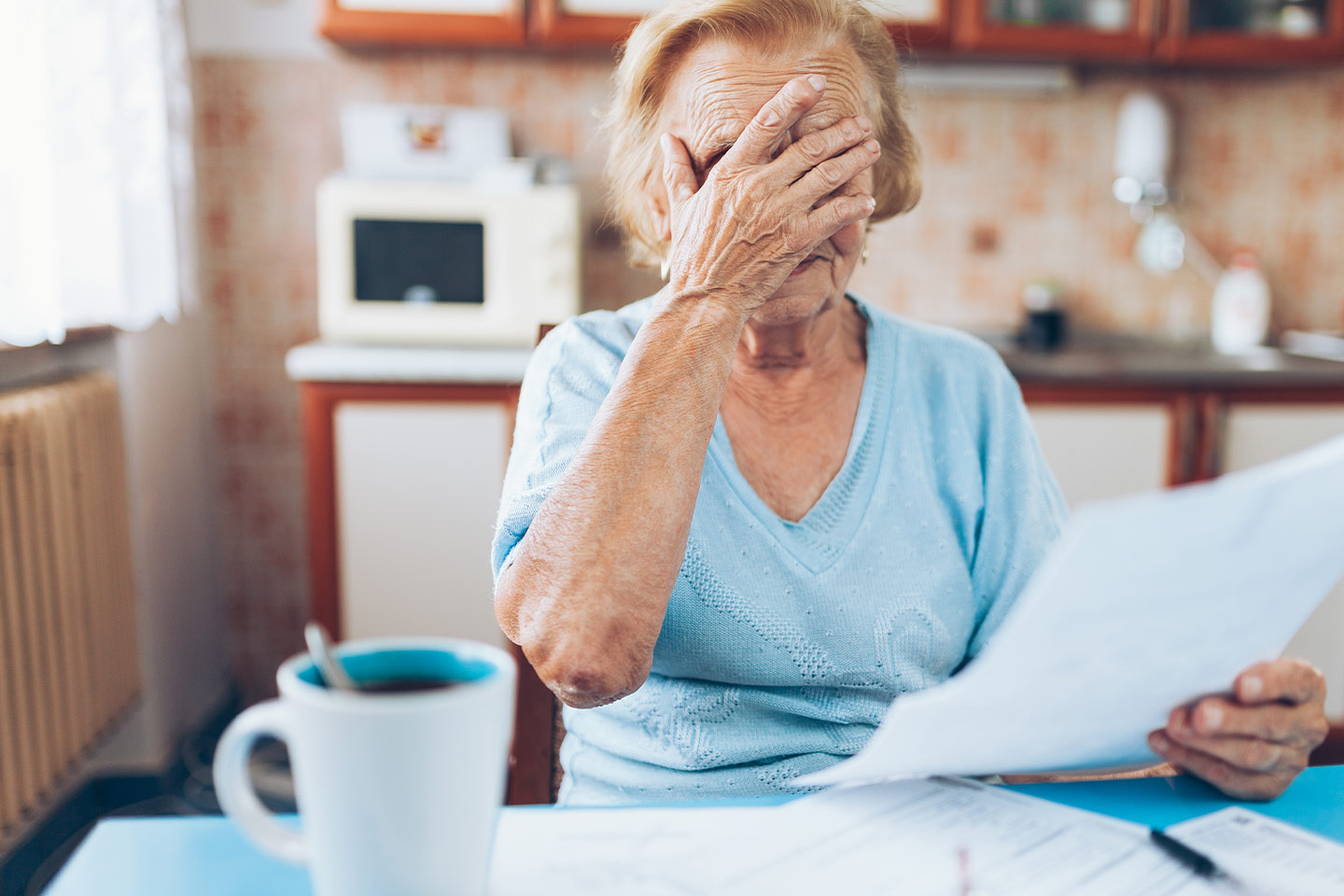 Photo of woman with hands over her eyes and paperwork in hand
