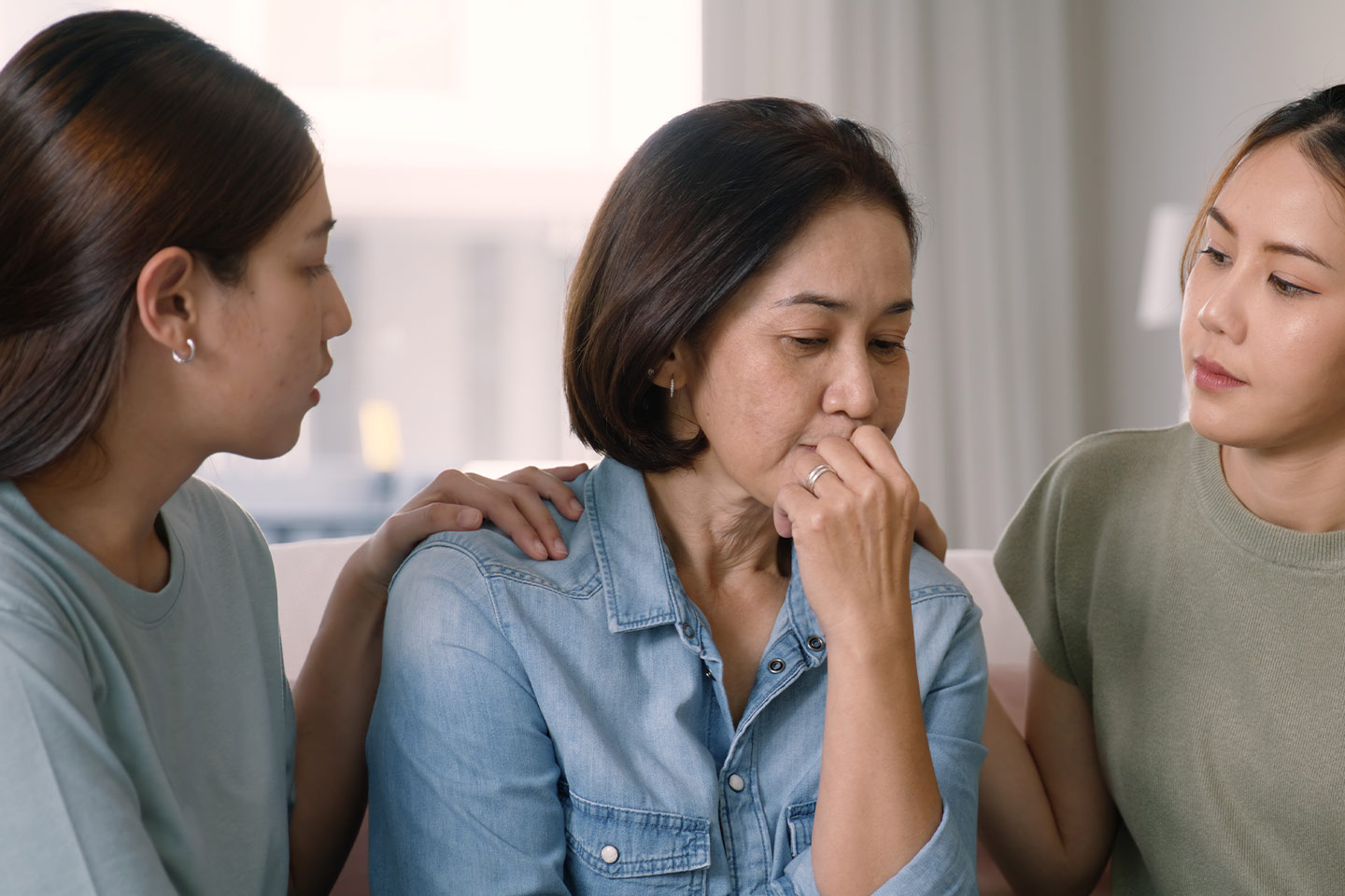 Photo of two women sitting either side of another woman and comforting her