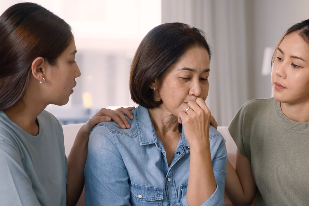 Photo of two women sitting either side of another woman and comforting her