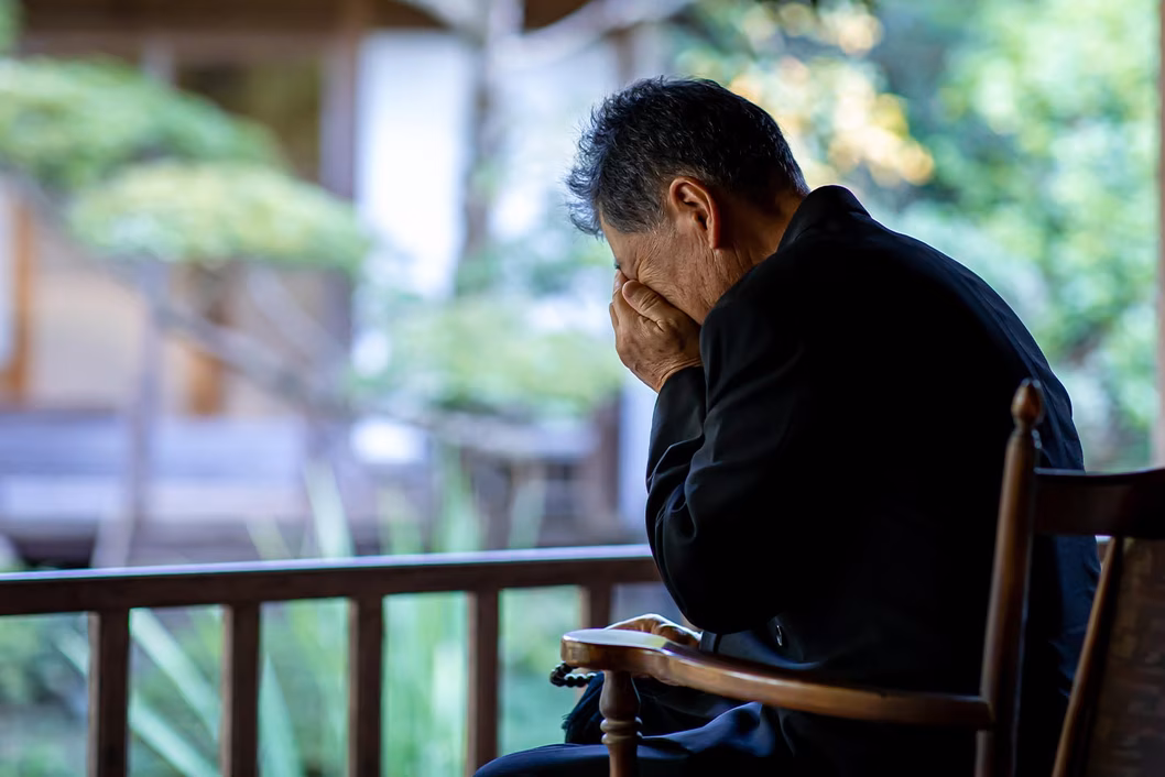 Photo of man with head in hands sitting on a verandah