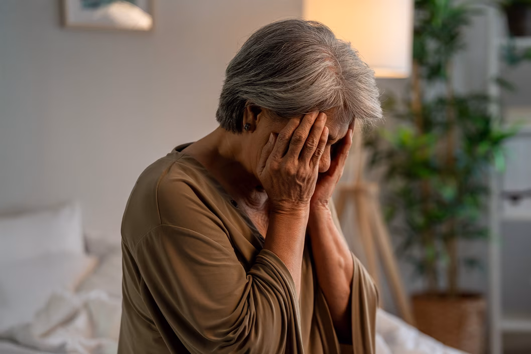 Image of an older woman who is distressed, resting her head in both hands