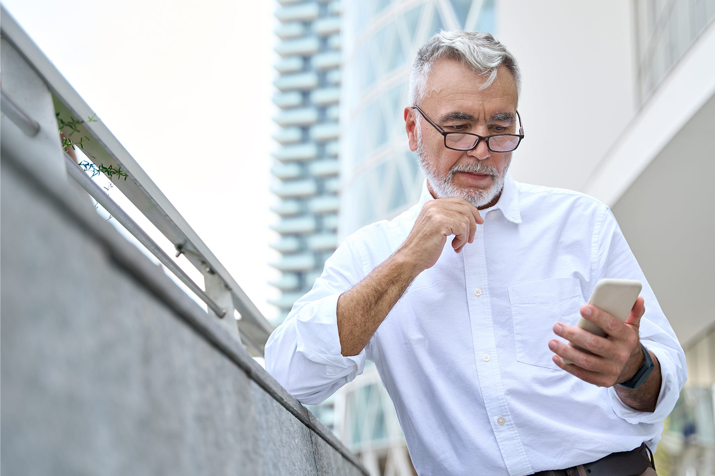 Photo of a man with a white beard and shirt looking at his phone
