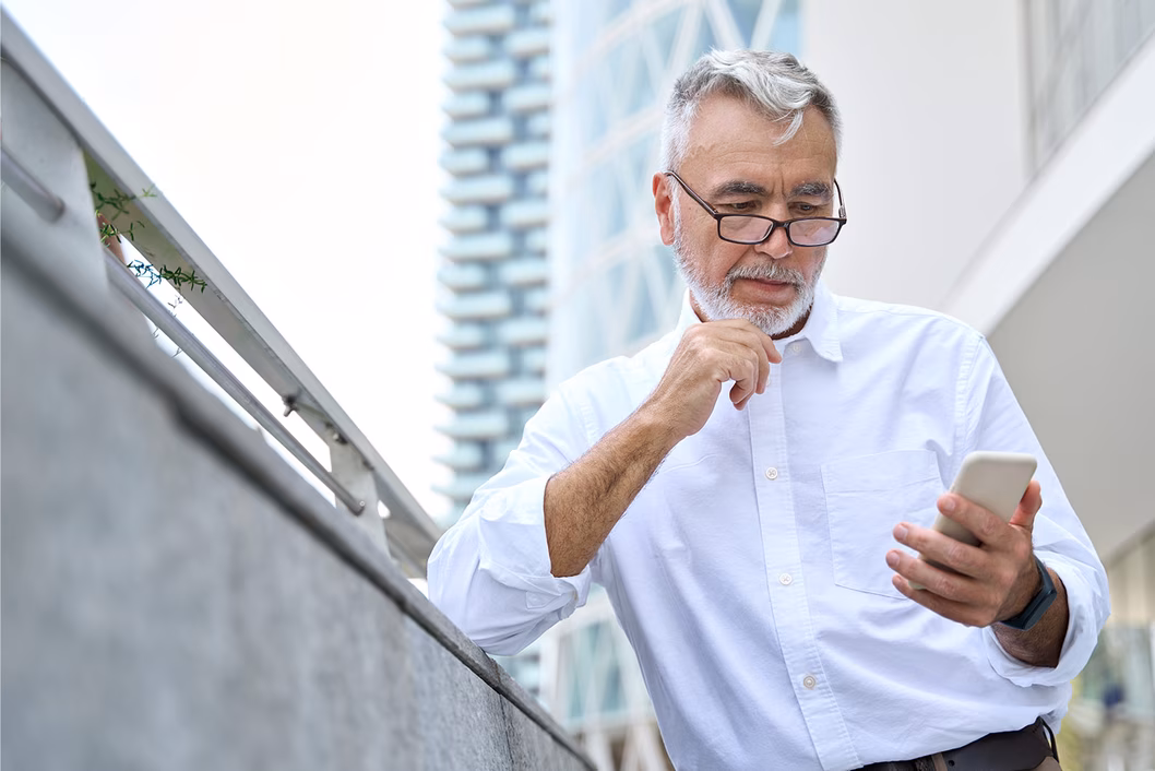 Photo of a man with a white beard and shirt looking at his phone