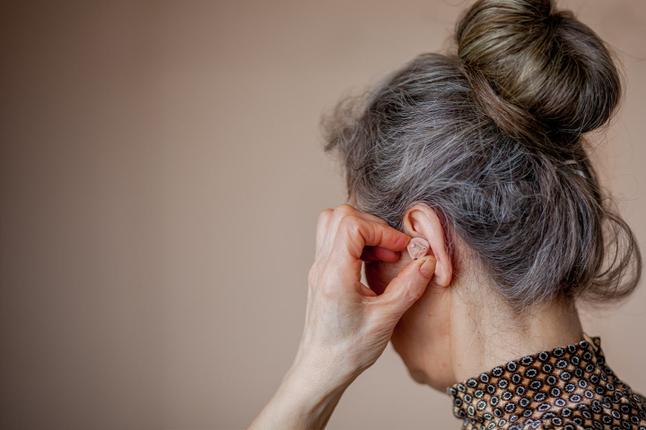 Image of an older woman placing a hearing aid into her left ear