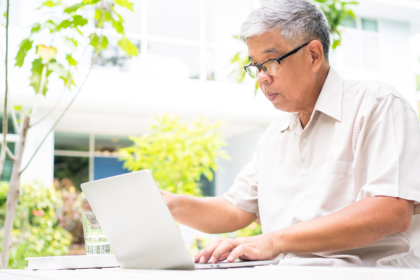 Older Asian man in glasses working at laptop computer