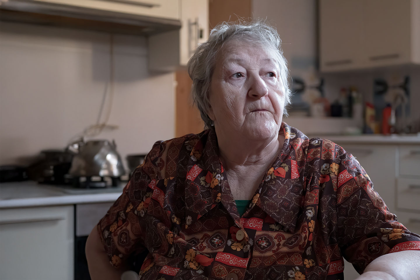 Image of an older woman sitting in her kitchen alone