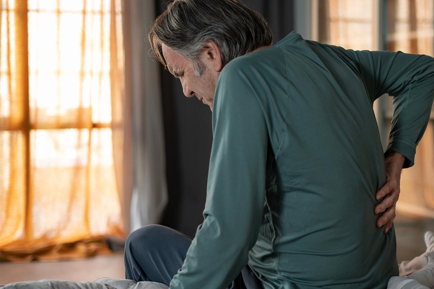 Photo of a man in a green shirt with his hand on his lower back
