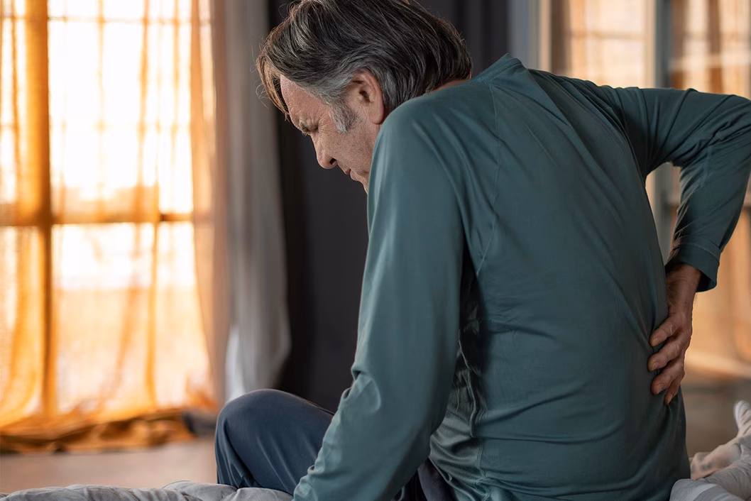 Photo of a man in a green shirt with his hand on his lower back