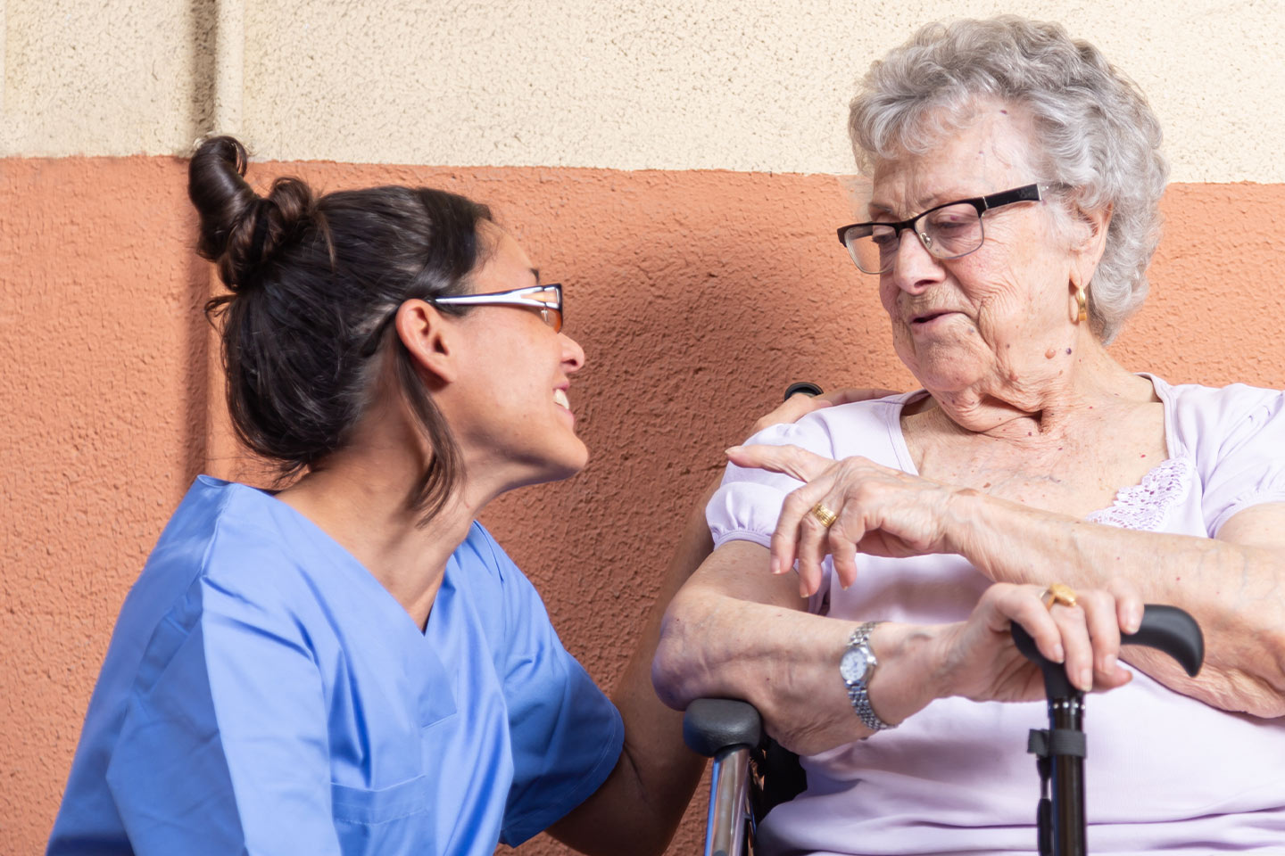 Photo of older woman talking with nurse in blue scrubs