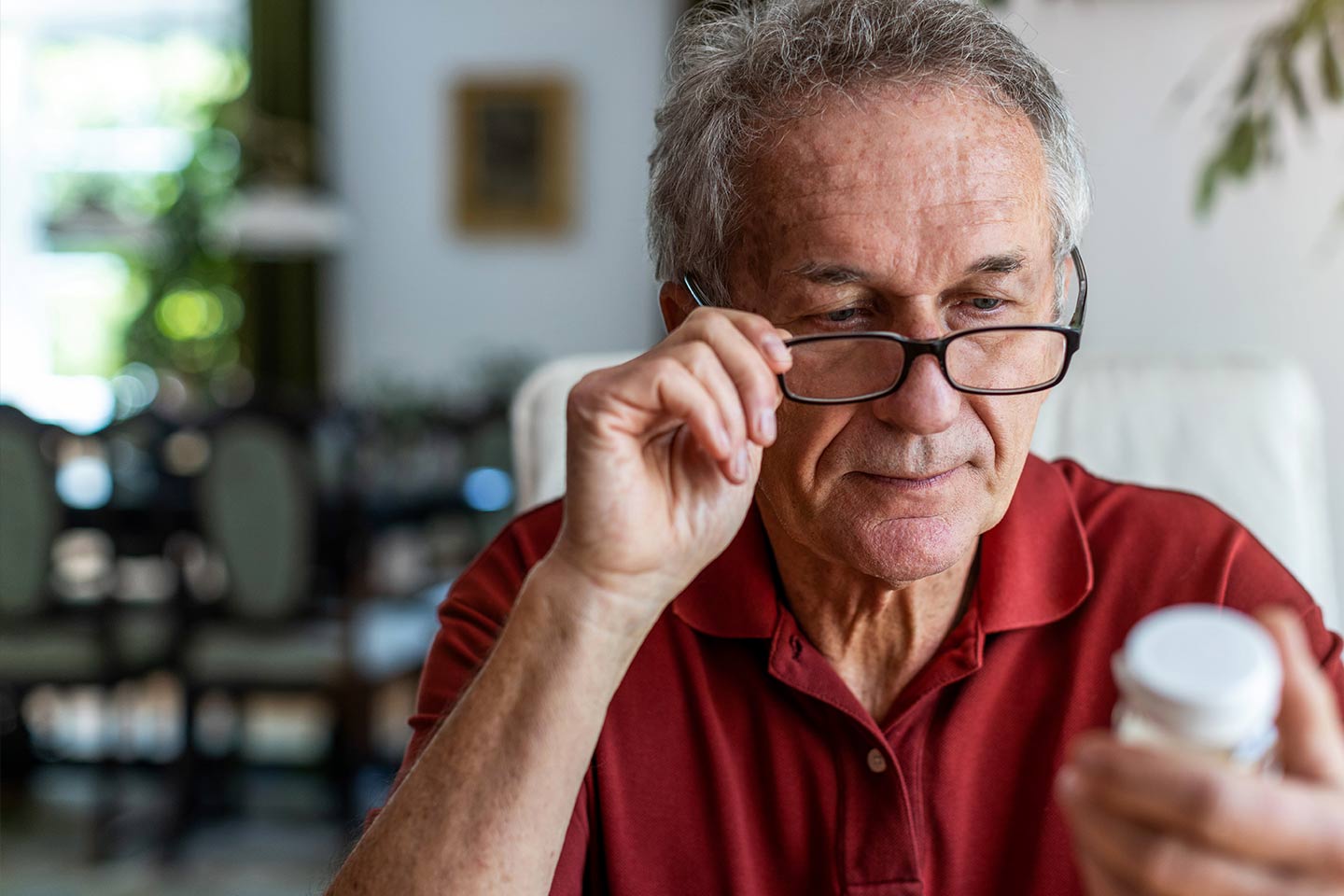 Photo of a man in a red polo looking at a bottle of pills