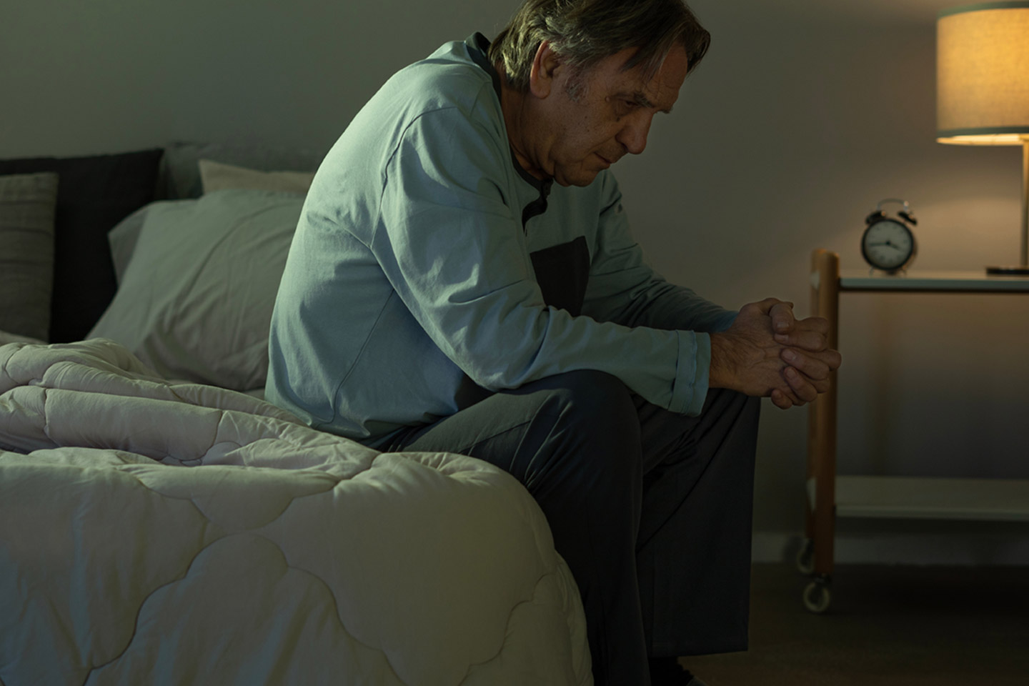 Older man sitting on his bed during the night looking unwell