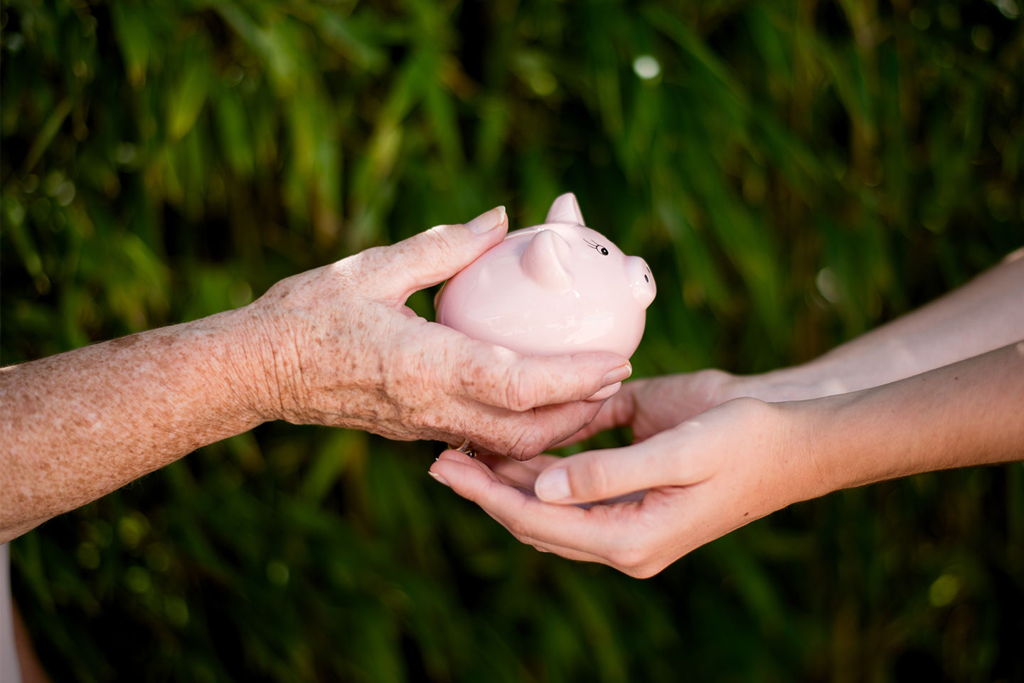 Photo of older hands giving piggy bank to younger hands