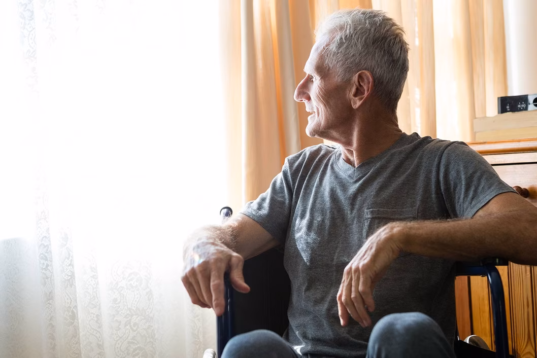 Photo of a man in a t shirt looking out a window