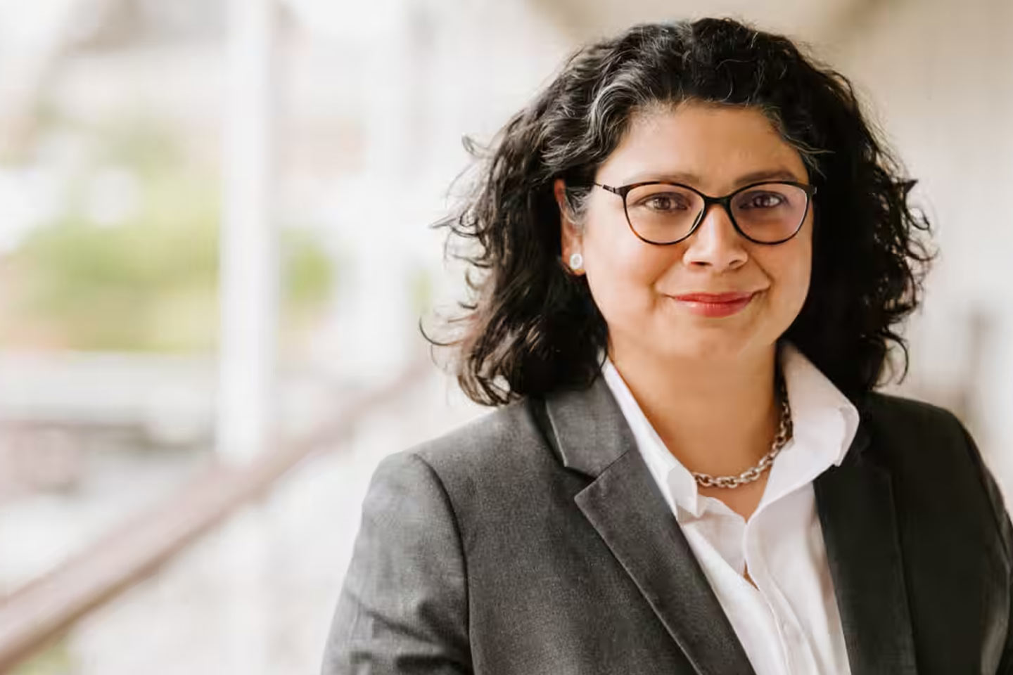 Photo of a smiling woman in a grey suit jacket and black glasses