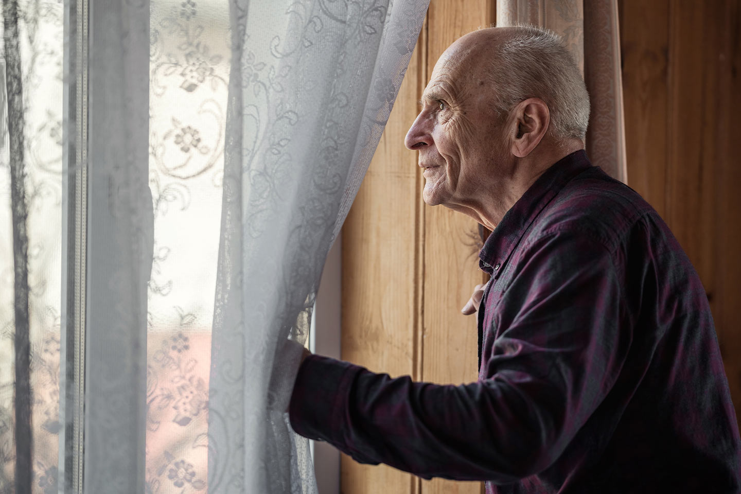 Photo of a man looking through a curtained window