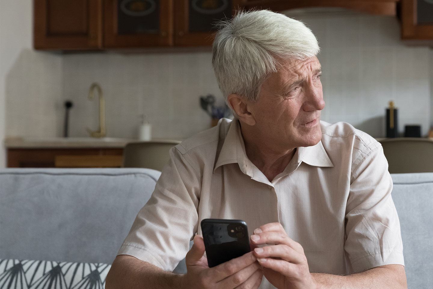 Image of an older man sitting on a sofa and holding a mobile phone