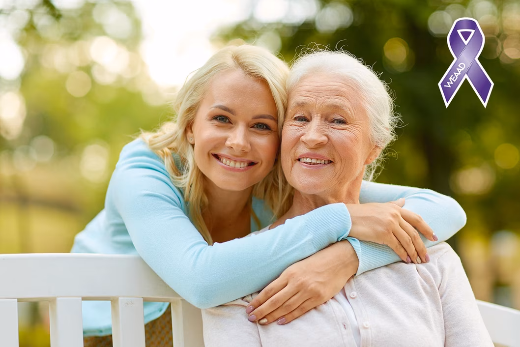 Photo of a woman in a blue cardigan embracing another woman on a park bench