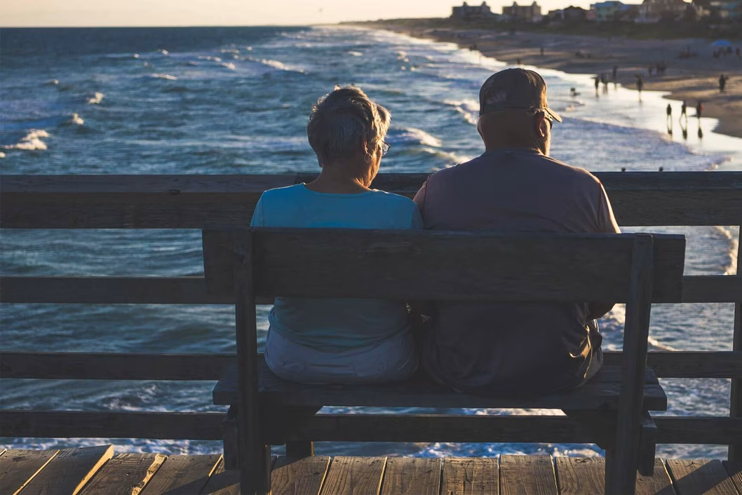 Photo of two people sitting on a bench overlooking a beach