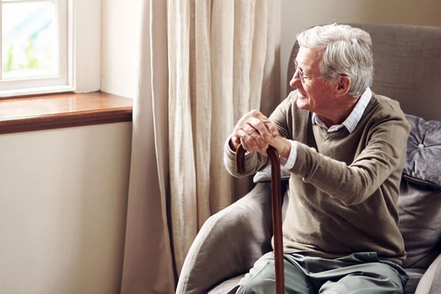 Photo of a man with a walking stick looking out a window