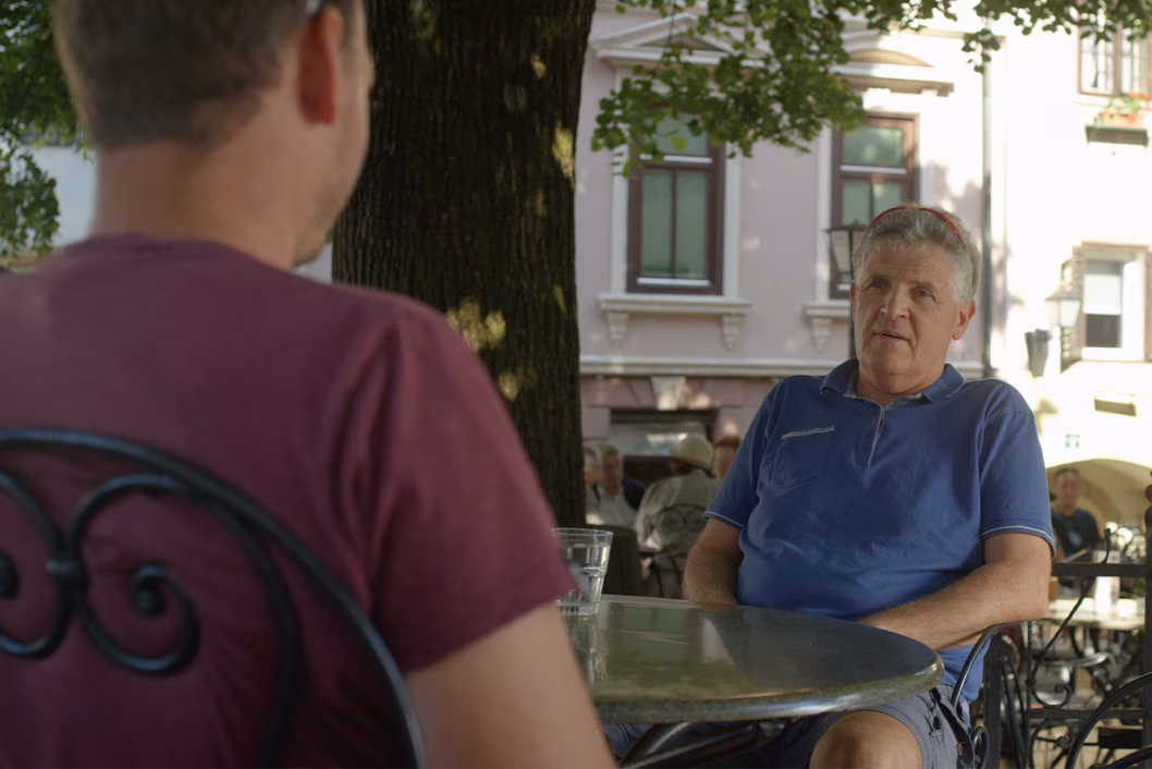 Photo of two men sitting under a tree at a cafe table