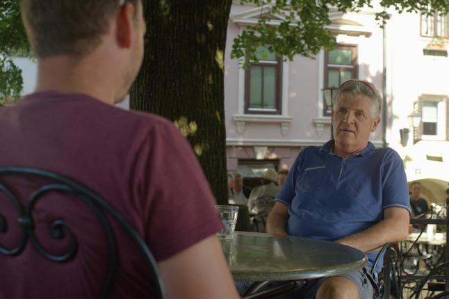Photo of two men sitting under a tree at a cafe table