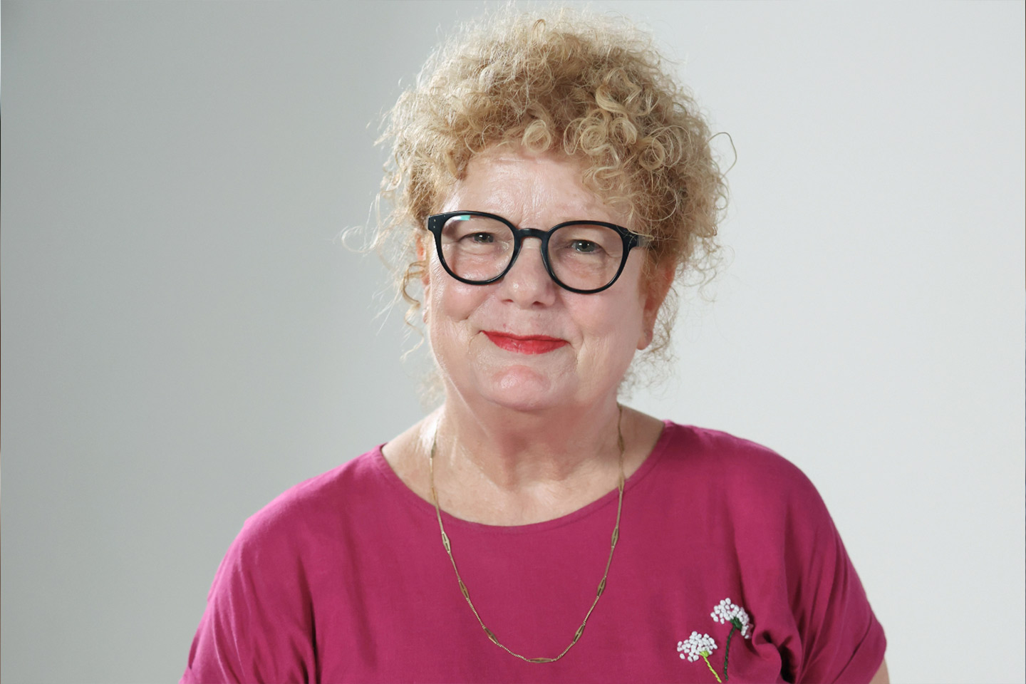 Photo of a smiling woman in a magenta shirt and black glasses