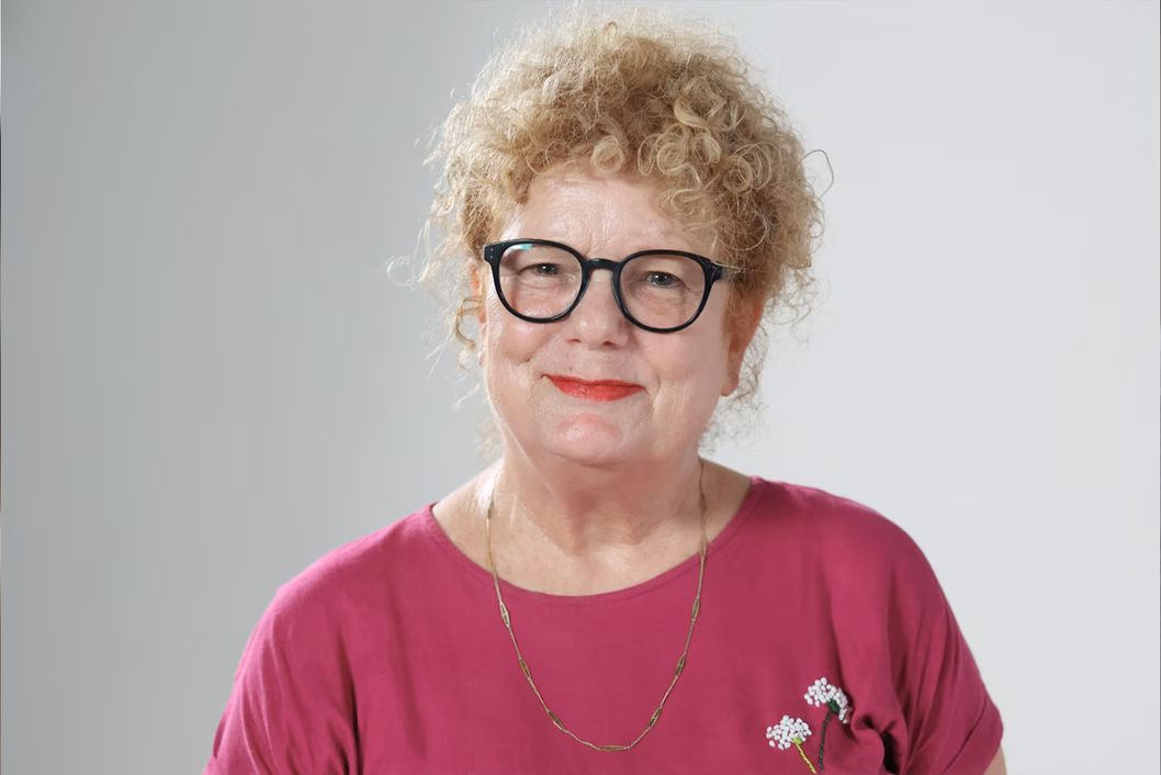 Photo of a smiling woman in a magenta shirt and black glasses