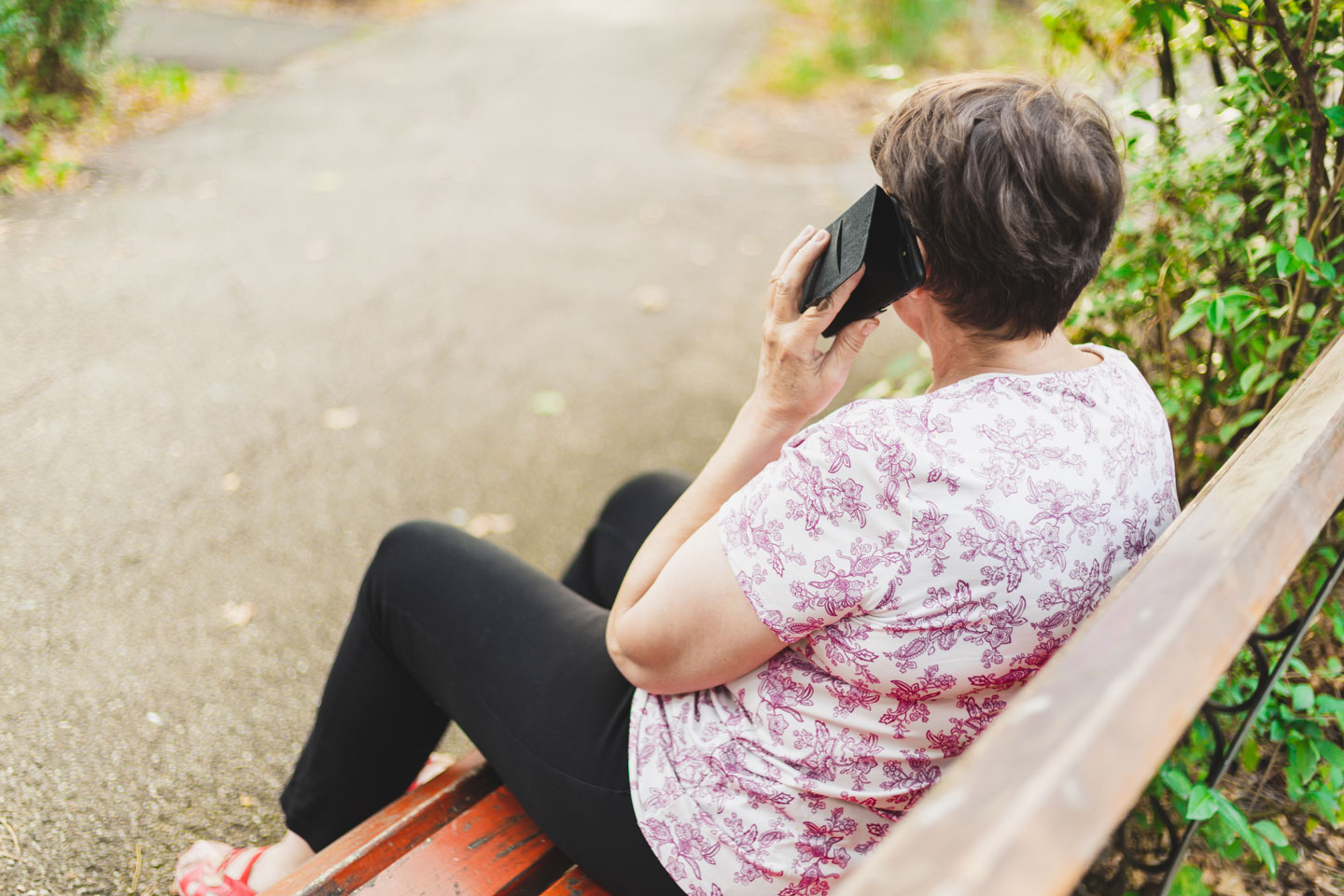 Senior woman sitting on a park bench and talking on the phone