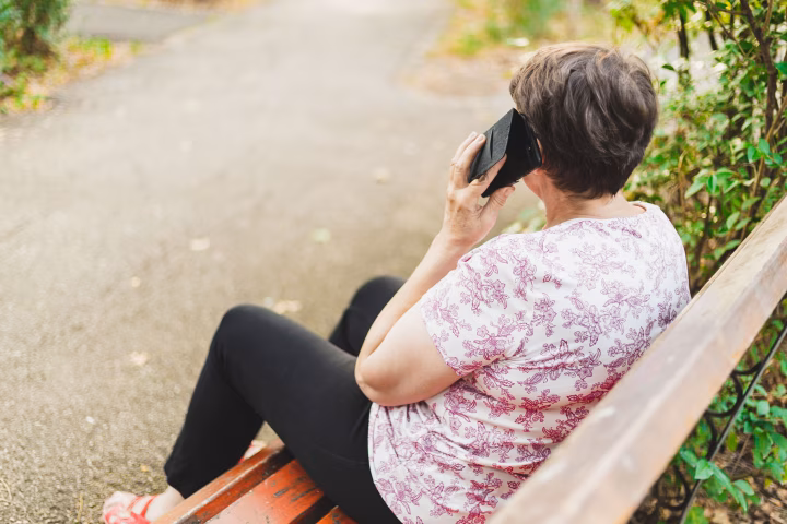 Senior woman sitting on a park bench and talking on the phone