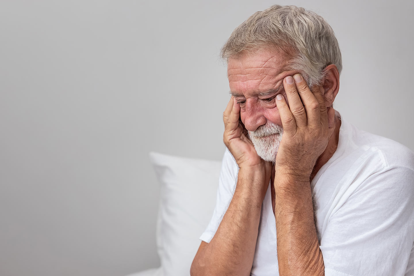 Photo of a man in a white T-shirt rubbing his temples