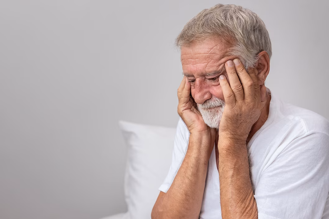 Photo of a man in a white T-shirt rubbing his temples