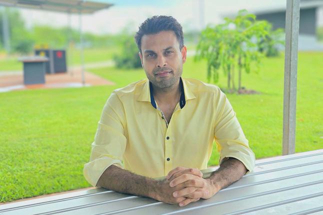 Photo of a man in a yellow shirt sitting at an outdoor table