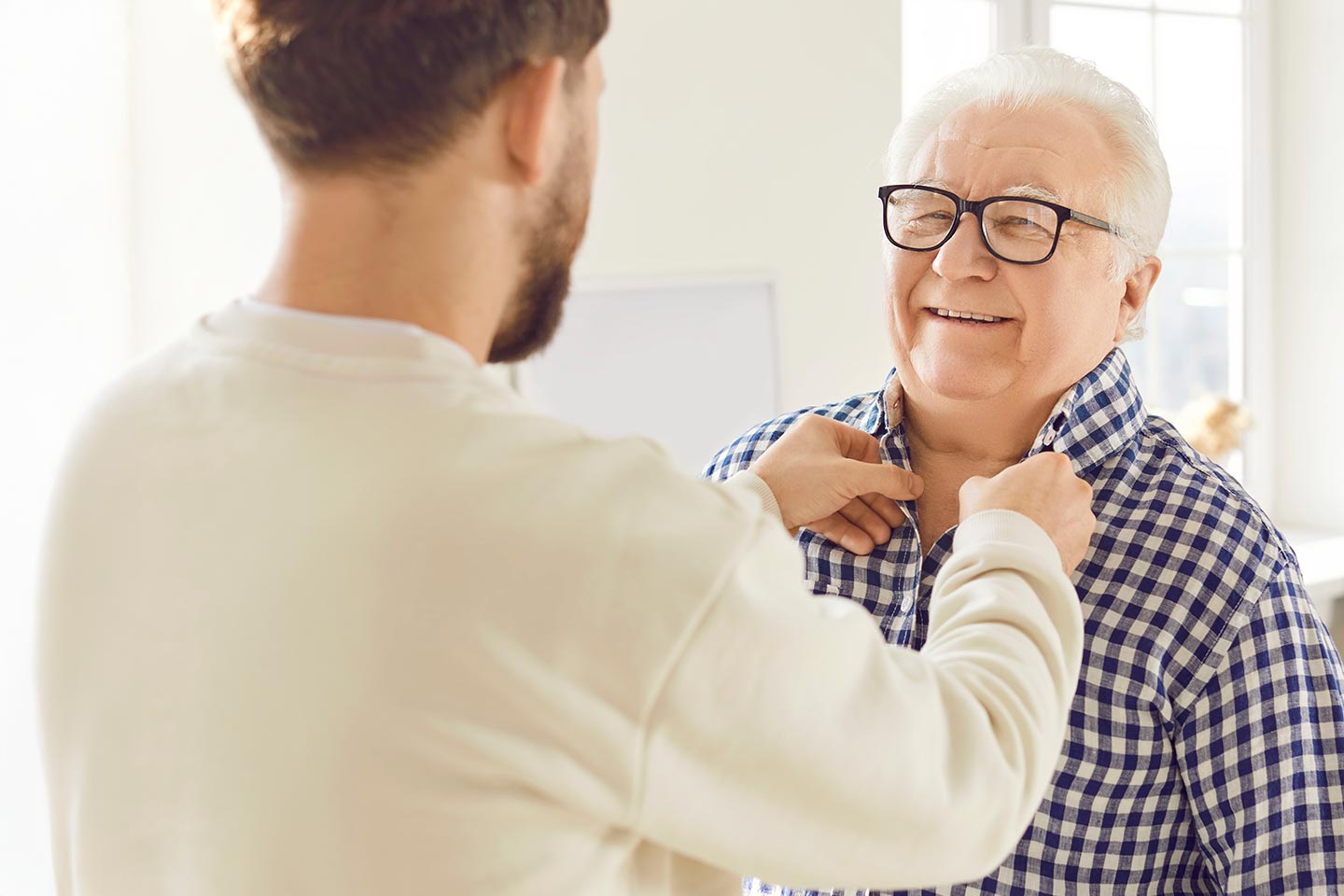 Photo of a bearded man doing up the buttons of another man's shirt