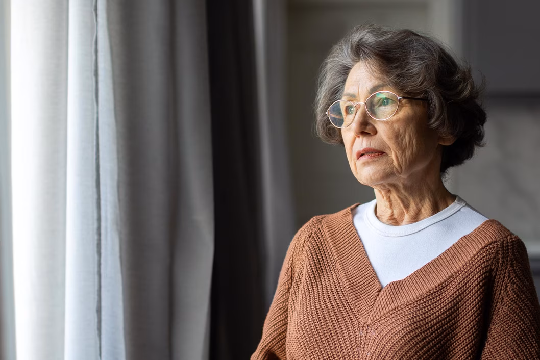 Photo of woman looking pensively through window