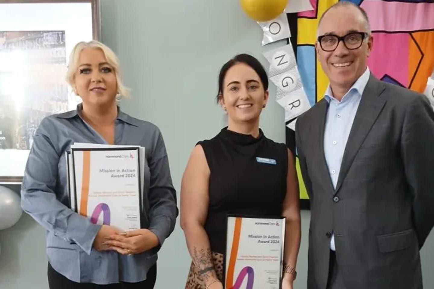 Photo of two women holding certificates standing next to a man