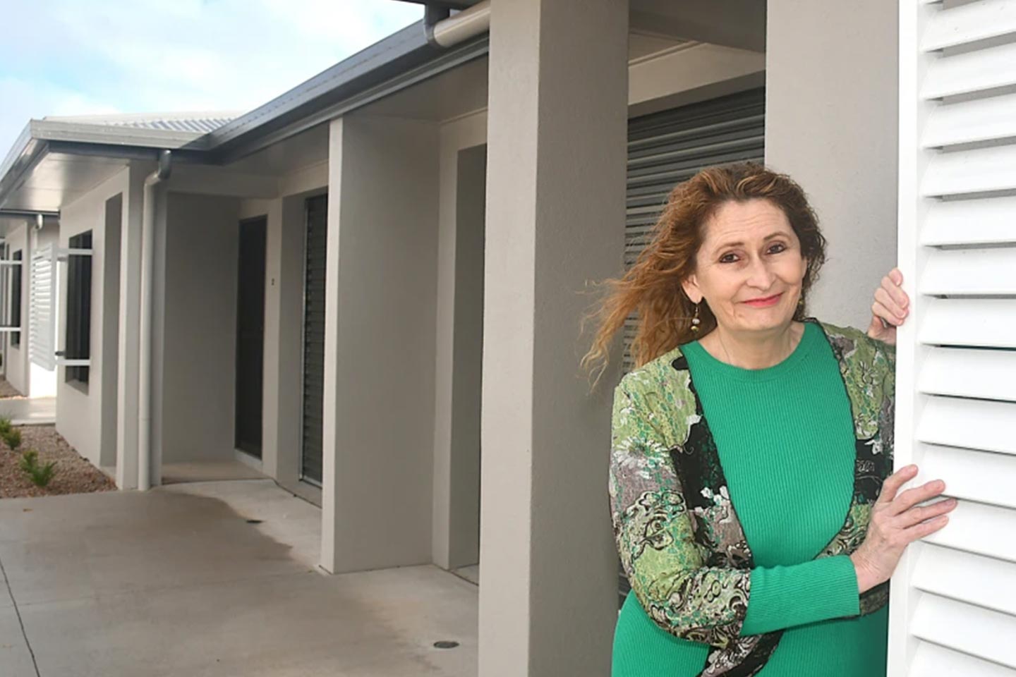 Photo of a woman in green smiling in front of a new home