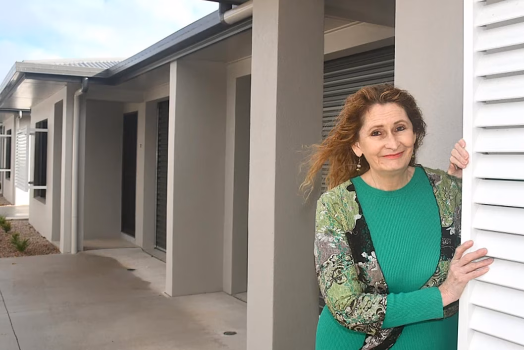 Photo of a woman in green smiling in front of a new home