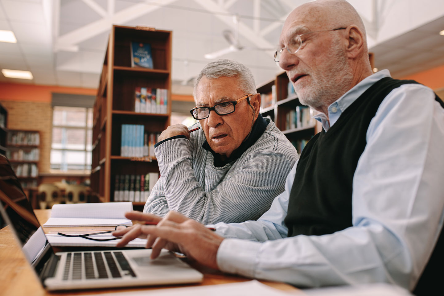Photo of two men in a library looking at a laptop